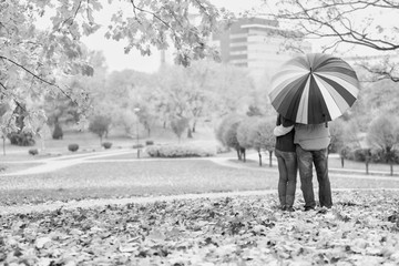 Black and white photo of man holding umbrella while enjoying the lovely view with his wife in park