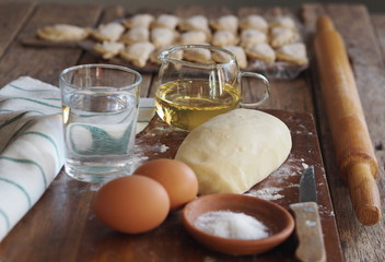 Wooden background with dumplings and dough ingredients for making dumplings. Food and cooking utensils on a brown kitchen board. Place for text. The concept of cooking dough.