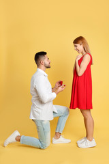 Man with engagement ring making marriage proposal to girlfriend on yellow background