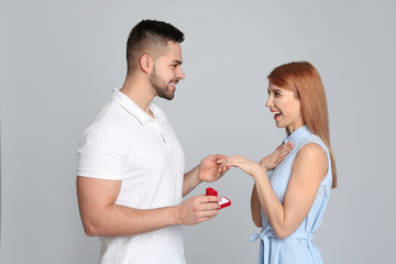 Man with engagement ring making marriage proposal to girlfriend on light grey background