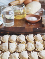 Wooden background with dumplings and dough ingredients for making dumplings. Food and cooking utensils on a brown kitchen board. Place for text. The concept of cooking dough.