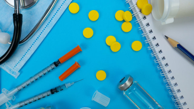 Syringe for Insection, Yellow tablets and Stethoscope As Background. Vaccine and paper notebook. Concept of clinic or hospital, health care or doctor. Medical Equipment on blue surface