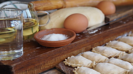 Wooden background with dumplings and dough ingredients for making dumplings. Food and cooking utensils on a brown kitchen board. Place for text. The concept of cooking dough.