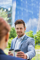 Portrait of young attractive businessman giving coffee to businesswoman