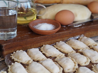 Wooden background with dumplings and dough ingredients for making dumplings. Food and cooking utensils on a brown kitchen board. Place for text. The concept of cooking dough.