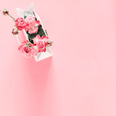 Flowers composition minimal. Pink rose flowers in white paper bag on pastel pink background. Valentines Day. Birthday, Happy Women's Day. Flat lay, top view, copy space, square