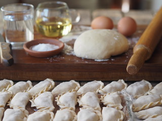 Wooden background with dumplings and dough ingredients for making dumplings. Food and cooking utensils on a brown kitchen board. Place for text. The concept of cooking dough.