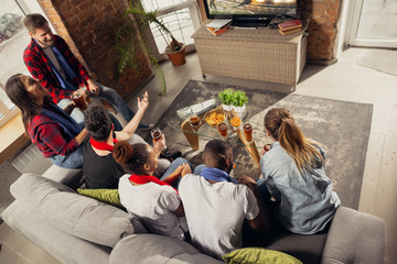 Excited group of people watching rugby, sport match at home. Multiethnic group of emotional friend, fans cheering for favourite national team, drinking beer. Concept of emotions, support, enjoyment.