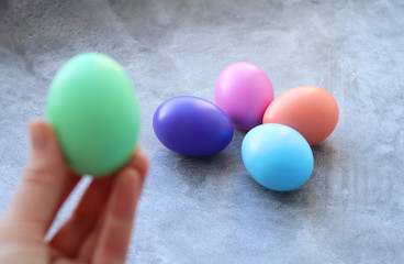 Easter eggs in beautiful pastel colors. The green egg in the hand is out of focus, the other eggs on the gray concrete background are in focus. Selective focus