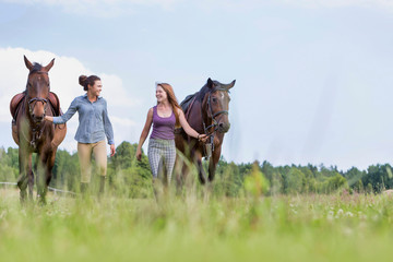 Portrait of women walking while talking with their horses in ranch