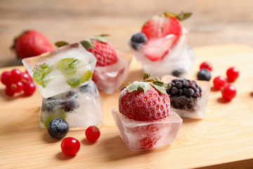 Ice cubes with different berries and mint on wooden board, closeup