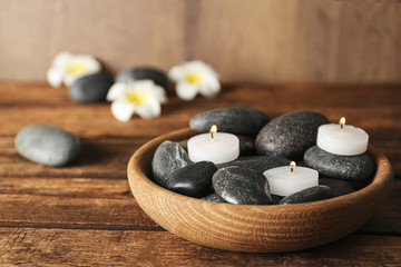 Fototapeta na wymiar Wooden bowl with burning candles and spa stones on table