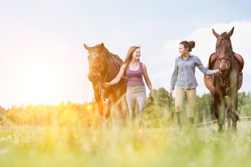 Portrait of women walking while talking with their horses in ranch