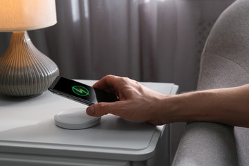 Man putting smartphone on wireless charger in room, closeup