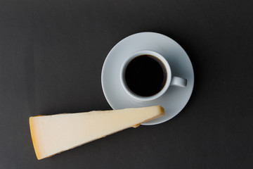 A small Cup of black coffee with a large piece of cheese. Top view.