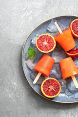 Close-up red orange popsicles with ice and mint leaves on a plate, gray concrete background. Top view, flat lay