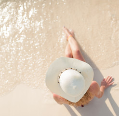 young lovely girl sitting with relaxing and happiness on the beachpretty woman in white hat posing in the sea. Attractive fashionable woman having fun on the beach. Blue sky, hair wild, outdoor portra