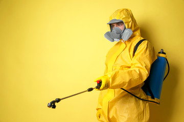 Man wearing protective suit with insecticide sprayer on yellow background, space for text. Pest...