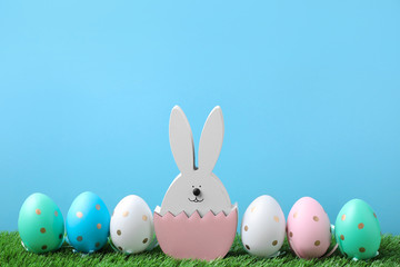 Easter bunny figure and dyed eggs on green grass against light blue background