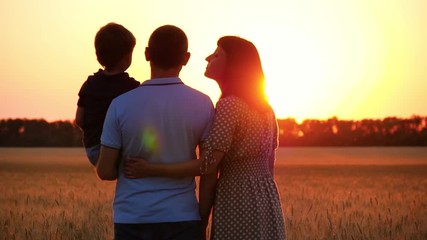 The family stands in a wheat field and enjoys the sunset. A man father holds his son in his arms, a woman mother hugs her man and kisses him. A child kisses his father. The concept of a happy family