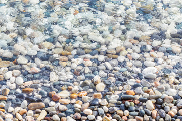 Sea coast covered with colorful pebbles. Soft transparent wave, marine background.