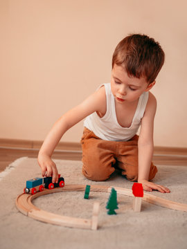 Small boy makes a choo-choo train with mouth while sitting on the floor and playing with a wooden train toy