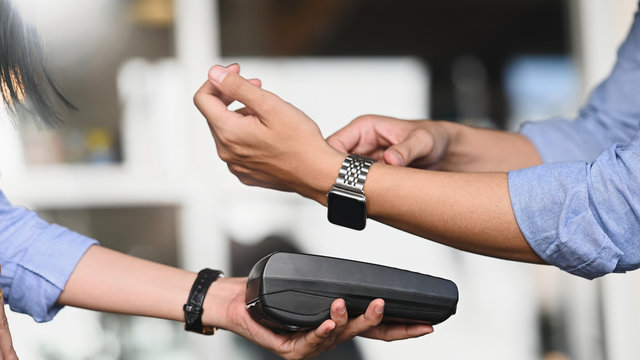 Cropped image of Businessman making a payment by using a smart-watch with blurred cafe/restaurant as background. NFC technology concept.