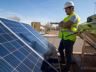 Caucasian attractive young technician looking at the solar panels with a glass cleaner wiper in his hand