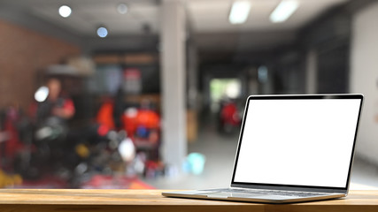 Obraz premium Computer laptop with empty white screen putting on modern wooden table in blurred garage as background.
