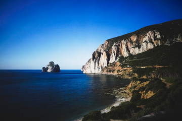 Panoramic view of the coast line with a sugar loaf monumental rock and a cliff falling into the sea in a bright sunny day.