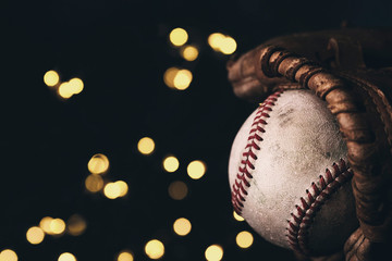 Baseball in glove closeup with blurred bokeh lights on black background.