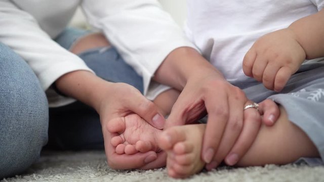 Mother making gentle feet massage to barefoot baby while sitting on floor at home