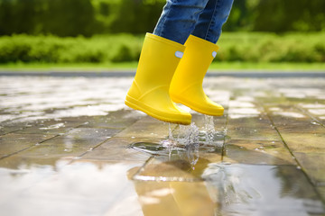 Little boy jumping in puddle of water at the summer or autumn day