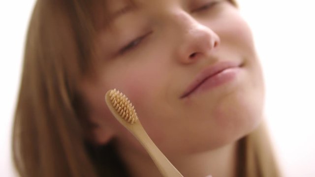 Bamboo wooden toothbrush in the hands of a beautiful woman. Eco-friendly zero waste oral hygiene tool. Slow motion with selective soft focus