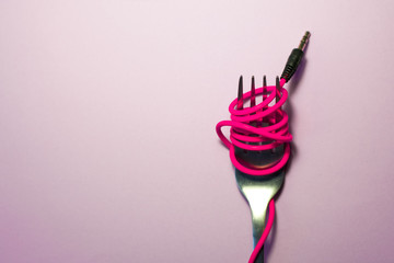 Pink background. Red, pink, yellow headphone cable is wound on silver fork. Spaghetti.