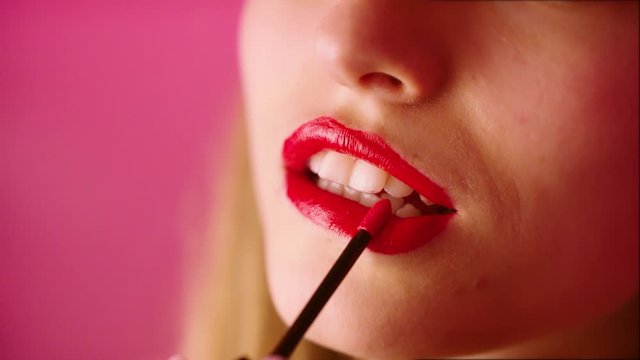A lovely female model applying a red lipstick color on both lips - closeup shot