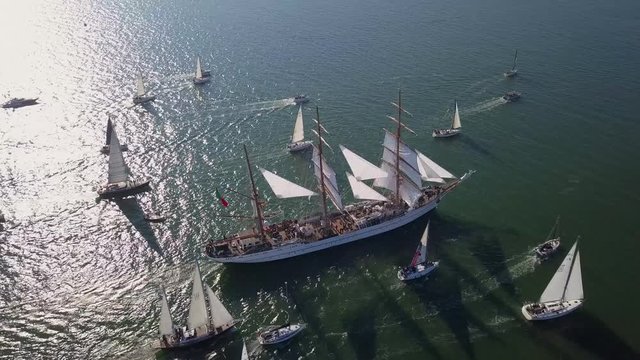 Aerial, orbit, drone shot of a old barque ship, surrounded by a fleet of boats, on Tagus river, sunny day, in Lisbon, Portugal