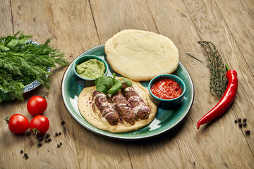 Appetizing rolls of Lyulya kebab - cooked over a lamb minced meat with a side dish of hummus with pita and salsa on ceramic plate. Vertical, wooden background, Eastern cuisine