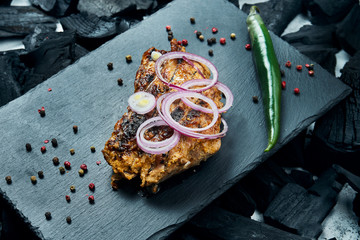 Appetizing chicken kebab with spices and onions on a black slate tray on a background of charcoal. Shahlik. Close up portion of grilled meat