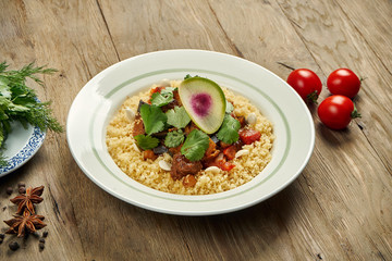 Dietary porridge couscous with grilled lamb and vegetables in a white plate on a wooden background. Eastern cuisine, close up, horizontal
