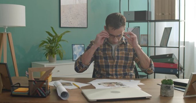 Caucasian man interior designer taking on glasses and working with drafts and draws of the apartment planning and interior.