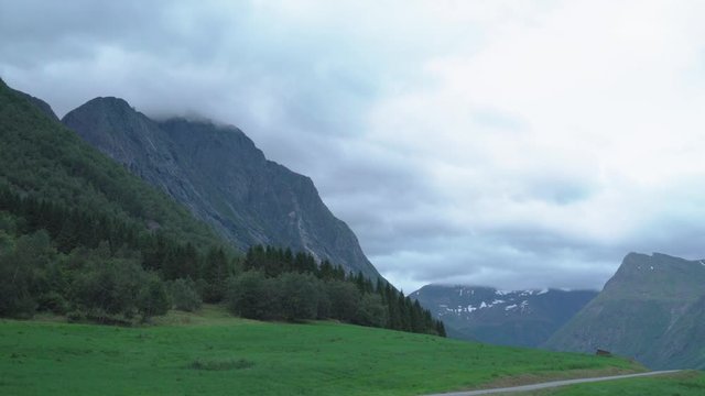 White clouds passing fast over mountain top - green meadows below, real time footage