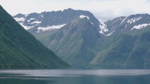 high mountains with snow in a norwegian fjord on a cloudy day -static shot no people