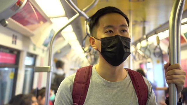 Close up of one young Asian man wearing a black surgical face mask in subway train during new type Coronavirus Covid-19 pneumonia outbreak and pm 2.5 smog air pollution crisis in big city.