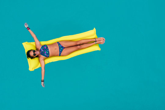 Woman in bikini on the inflatable yellow mattress in the swimming pool.