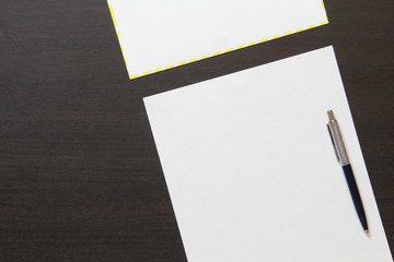 Template of white paper with pen and envelope on dark wenge color wooden background.