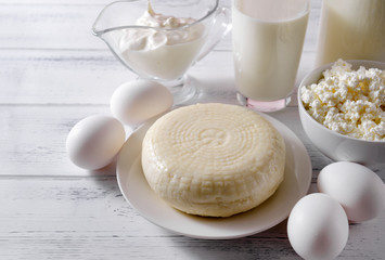 glass of milk, a bottle of milk, several raw eggs, cottage cheese, cheese, sour cream on a light wooden