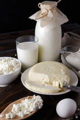 dairy products on a dark wooden background, a bottle of milk,  egg,  cottage cheese, cheese