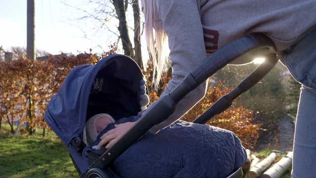 Female pushing pram stops to check baby is comfortable during walk