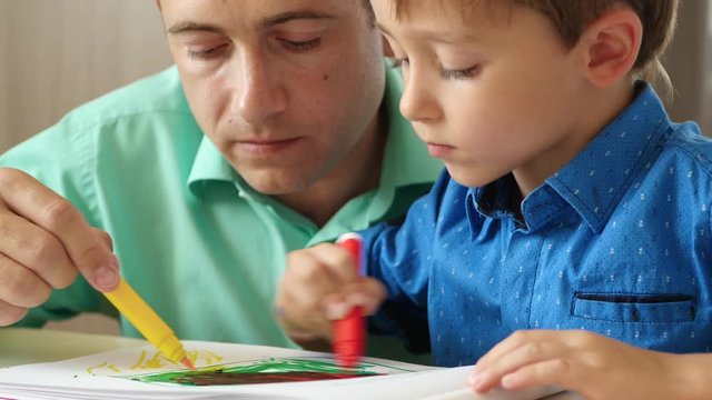 A mature father spends time with his young son, drawing with colored pencils.Close up. The concept of a happy family. Collaboration.
